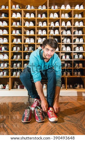 Man, sitting on a stool, trying on bowling shoes in front of wooden selves with an array of different sizes leather shoes