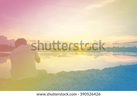 man sit down and take photo by camera at lake with sunset sky. Fill color filter.