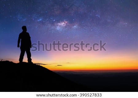 Silhouette of man is standing on top of mountain and enjoy to see the milky way before sunrise. Young tourist stand on the hill with colorful night sky on background. Royalty-Free Stock Photo #390527833