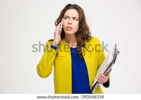 Portrait of pensive unpleased young woman with clipboad talking on mobile phone over white background