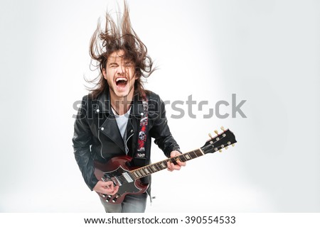 Excited young man in black leather jacket with electric guitar shouting and shaking head over white background Royalty-Free Stock Photo #390554533