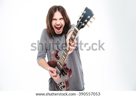 Excited popular young male singer with long hair shouting and playing electric guitar over white background