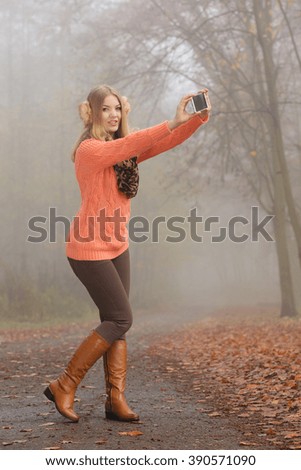 Happy fashion woman in fall autumn park taking selfie self photo picture. Pretty joyful young girl in sweater pullover and earmuffs photographing.