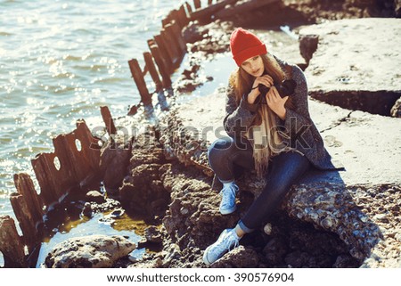 smiling young woman using a camera to take photo. Vintage processing. sea shore. hipster style clothing.