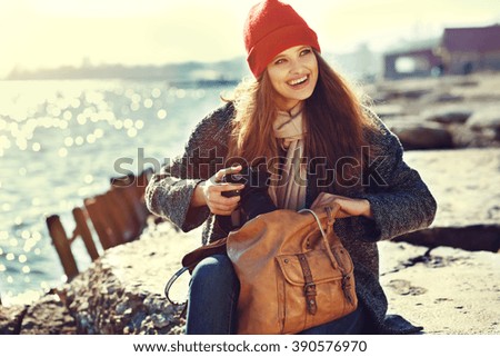 smiling young woman using a camera to take photo. Vintage processing. sea shore. hipster style clothing.