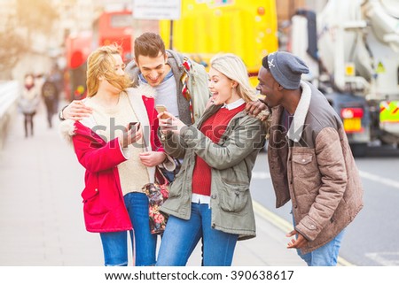 Group of young friends having fun in London. Mixed races people laughing and enjoying their time looking at a smart phone. Very candid and natural image with real expressions of happiness.