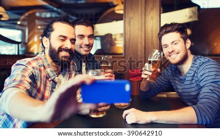 people, leisure, friendship, technology and bachelor party concept - happy male friends with smartphone taking selfie and drinking beer at bar or pub
