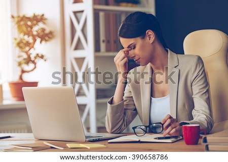 Feeling overworked. Frustrated young beautiful businesswoman looking exhausted while sitting at her working place and carrying her glasses in hand