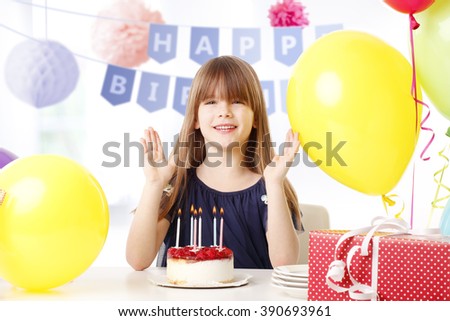 Portrait of adorable little girl celebration her birthday while sitting at desk behind her cake.
