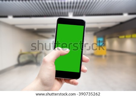 Hand uses a phone with a touch screen and place a copy in green. Airport terminal in fuzzy depth of field.