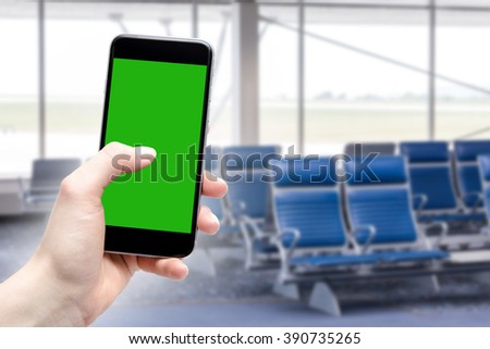 Hand uses a phone with a touch screen and place a copy in green. Airport terminal in fuzzy depth of field.
