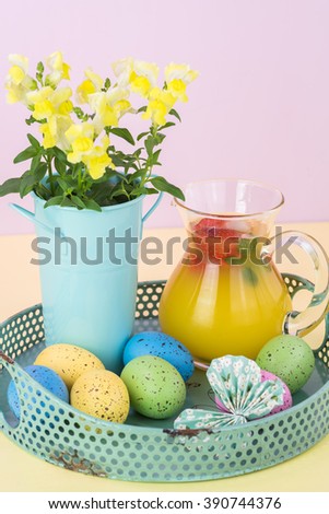 Close up of tray with pitcher of homemade strawberry orange blossom punch and easter eggs on pastel background.