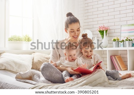 happy loving family. pretty young mother reading a book to her daughters Royalty-Free Stock Photo #390805201