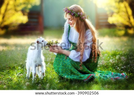 Beautiful smiling girl with long blonde shiny hair feeding a goat. Sun light. Glow sun.Romantic beauty female sitting in fantasy garden. Fairytale and art work.Amazing young model in vintage dress.
