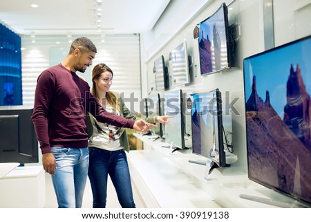 Couple in shopping. They are looking for new tv. They are pointing fingers at tv. Shallow depth of field. Royalty-Free Stock Photo #390919138