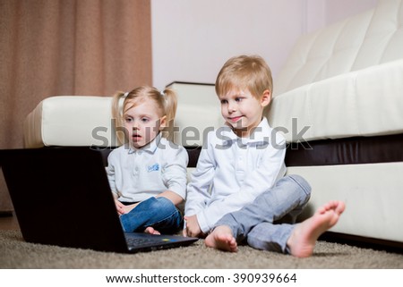 two children a boy and girl, brother and sister sitting on the floor in a white shirt and playing on the laptop and looking cartoon