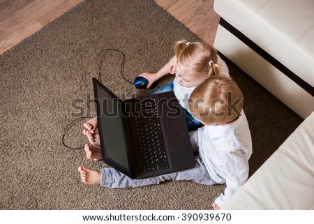 two children a boy and girl, brother and sister sitting on the floor in a white shirt and playing on the laptop and looking cartoon,view from above