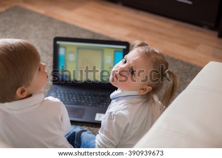 two children a boy and girl, brother and sister sitting on the floor in a white shirt and playing on the laptop and looking cartoon.girl is unhappy that her distracted