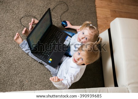 two children a boy and girl, brother and sister sitting on the floor in a white shirt and playing on the laptop and looking cartoon, view from above