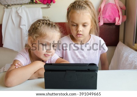 Two girls sisters sitting in the train watching cartoon Tablet PC