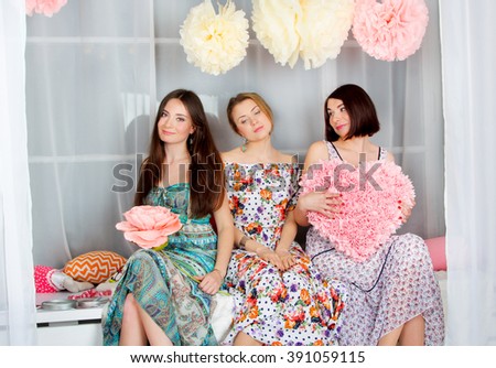 Young, beautiful and emotion girls in bright colored dresses. Decoration flowers and heart.  Spring mood - smile and antics. Girls gatherings. Portrait of attractive girls in the studio.