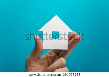 Hand holding white paper house figure on blue background. Real Estate Concept. Ecological building. Copy space top view.