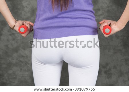Bottom of sports woman in white holding red dumbells standing with feet apart in sport hall training indoor closeup, vertical picture