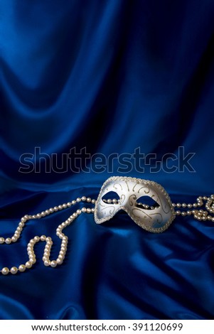 Silver carnival mask and pearl on dark blue silk background