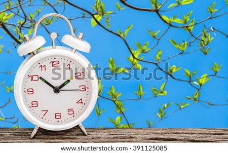 White alarm clock on wooden table with nature background soft focus.