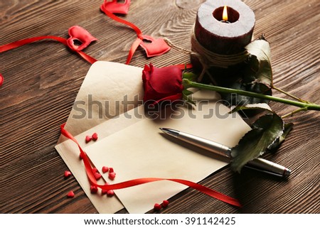 Gift card for Valentine's Day with red rose, pen and candle on wooden background