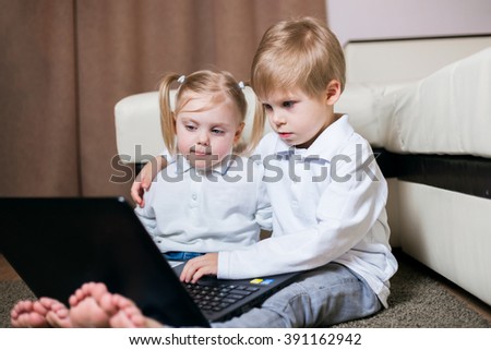 blond little children girl and boy in jeans sitting barefoot on the floor with a laptop watching cartoons, horizontal frame