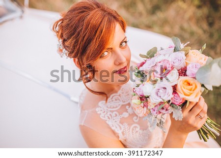 Fashion portrait of young bride with white dress with bouquet near retro car in autumn