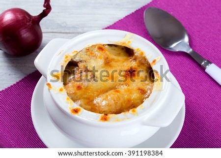 Delicious french onion gratin soup in a white pot, authentic recipe, spoon on a  napkin, selective focus, close-up