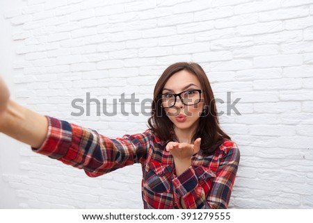 Girl Taking Selfie Photo Blowing Kiss Lips Smart Phone Camera Woman Posing Over White Brick Office Wall