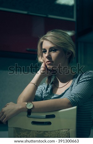 Young woman sitting alone and waiting at night on kitchen chair