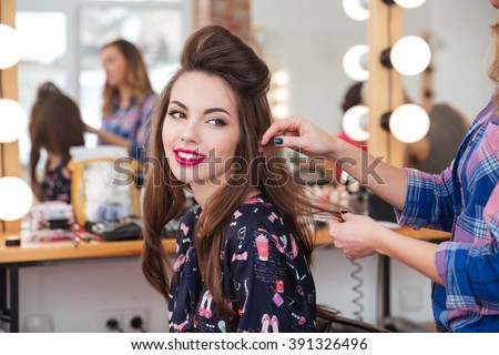 Female hairdresser standing and making hairstyle to cute lovely young woman in beauty salon Royalty-Free Stock Photo #391326496
