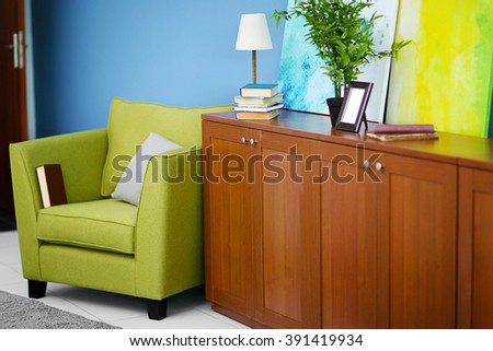 Living room interior with green armchair, commode and picture on blue wall background