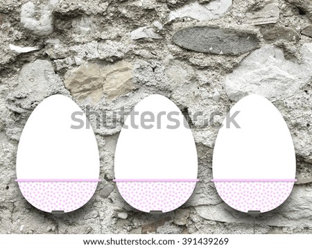Close-up of three hanged blank Easter egg frames with clips against grey stone wall 