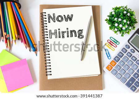Now hiring text message on white paper and office supplies, pen, paper note, on white desk , copy space / business concept / view from above, top view
