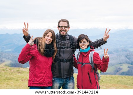 three young smiling friends hiking outside embracing and doing peace sign. Outdoor healhy happy lifestyle.