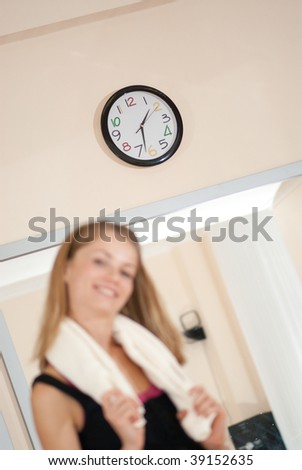 Young girl after fitness workout. Primary focus is on wall clock. Time concept
