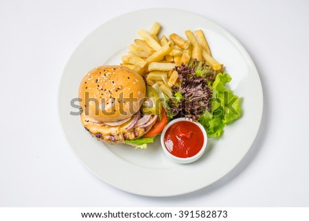 Burger with meat patty , cheese , onions, tomatoes , pickled cucumbers , green salad , potato chips and sauce . Close-up in white plate on a white background top view. Royalty-Free Stock Photo #391582873
