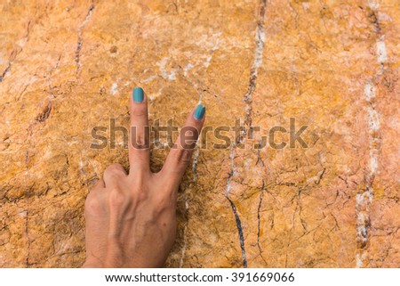 Woman hand holding up the peace sign or number two with two fingers on stone background texture