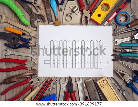 Tools on a wooden floor with a sketch of the fence on a sheet of paper in the center, top view. 