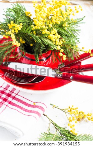 Spring festive dining table setting with yellow mimosa flowers, napkins and vintage cutlery on a white wooden board;