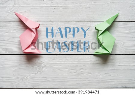 Happy Easter calligraphy. Paper origami handmade pink, green bunnies on white planks barn wood boards background. Space for text, lettering, copy. Easter holiday postcard template.