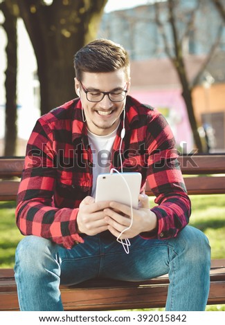 Young and handsome man with mobile tablet sitting in the park. Toned Image