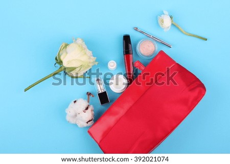 Beautiful make up bag with cosmetics and flowers on blue background