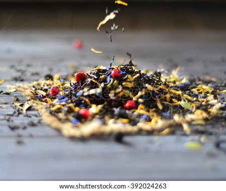 Dry Ceylon tea with berries - blueberries, raspberries, blackberries pours on a dark wooden table closeup