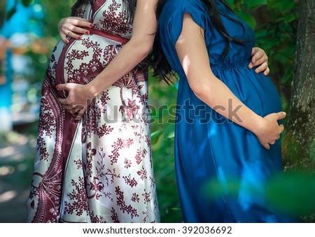 
two pregnant women holding hands on the tummy  Royalty-Free Stock Photo #392036692